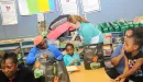 Thumbnail: An image of a Caucasian woman from the YMCA helping to teach African American mothers and daughters essential nutrition and cooking skills in a classroom.