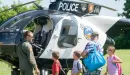 Thumbnail: An image of three Caucasian kids standing in front of a police helicopter with the pilot and their father, during the backpack give-away at the YMCA.