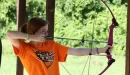 Thumbnail: girl pulls back a bow and arrow and aims, preparing to shoot a target