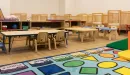 Thumbnail: Toddler room in Early Child Education Center. Small tables and chairs. Play structures and rugs. Infant cribs along back wall.