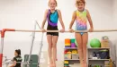 Thumbnail: two girls hang on the high bar in a ymca gymnastics program