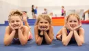 Thumbnail: three girls pose and smile in a ymca gymnastics class