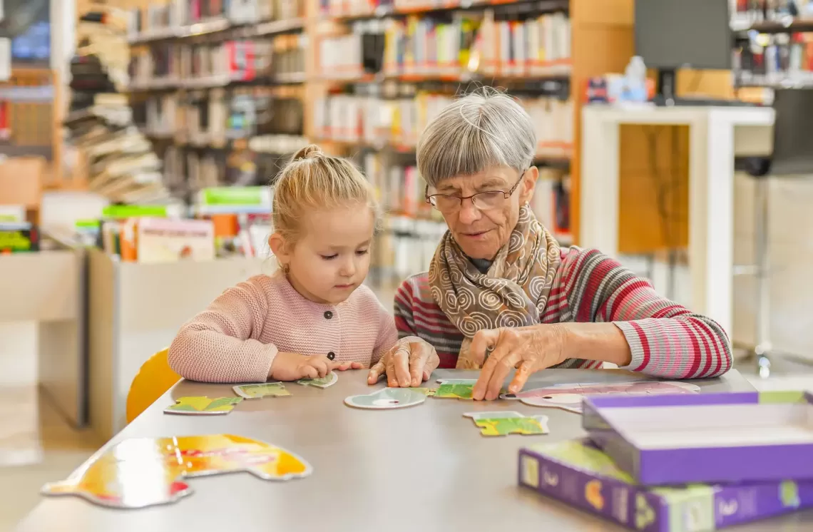 An image of a grandmother and granddaughter playing a matching game whilst sitting on the same side of a table and chairs at their local YMCA.