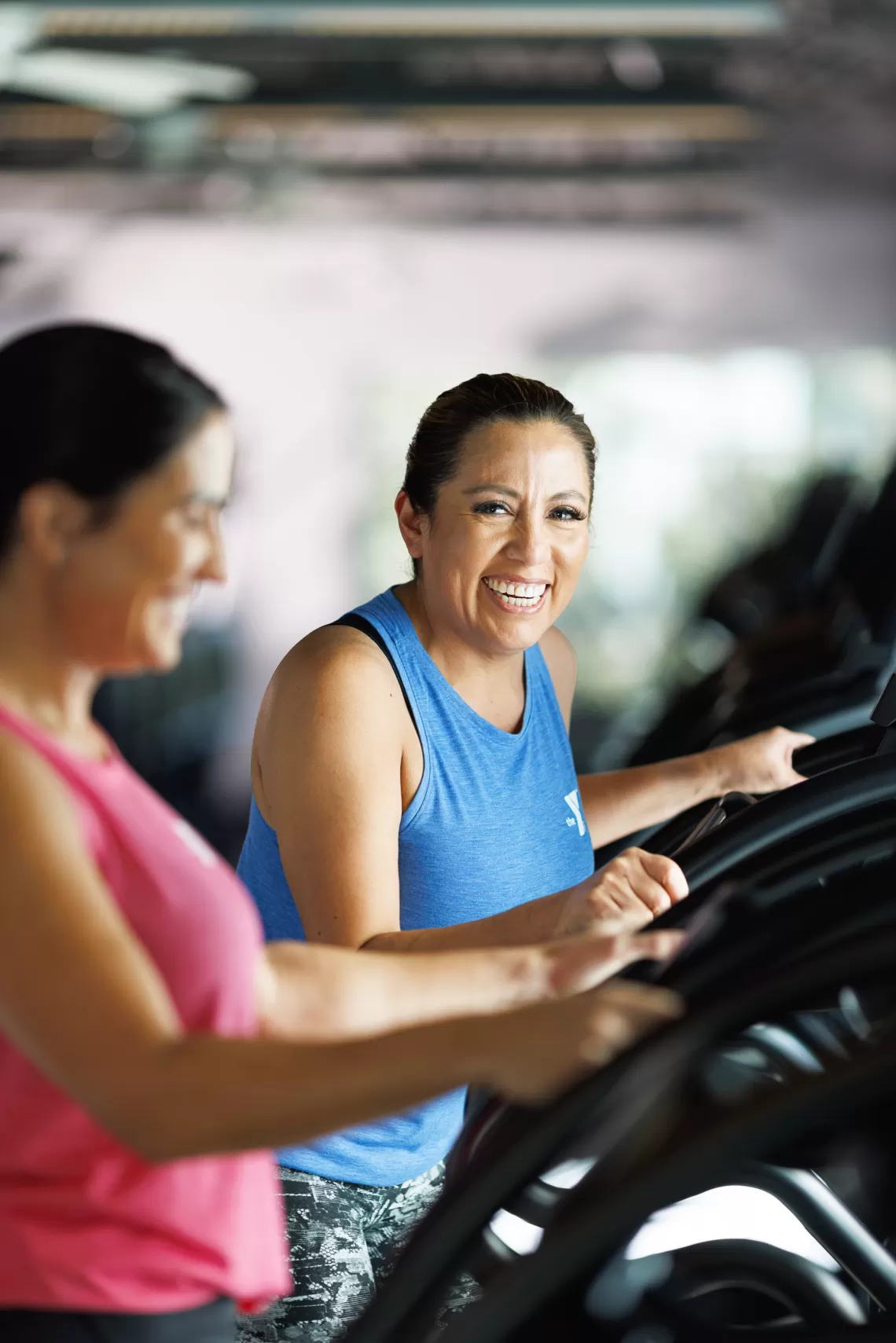 Two women working out on elliptical cardio machines in a YMCA fitness center