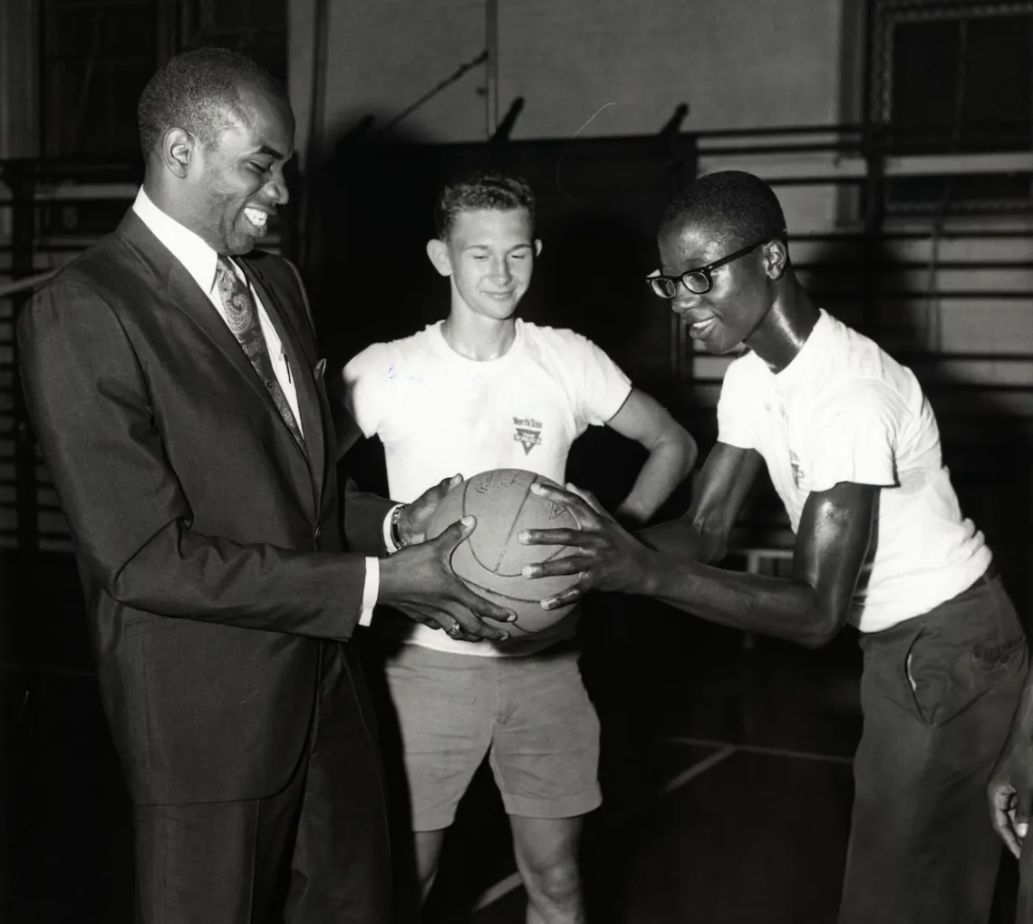 A historical photo of the Gateway Region YMCA association's Downtown St. Louis YMCA location with a coach and young basketball participant in the gymnasium.