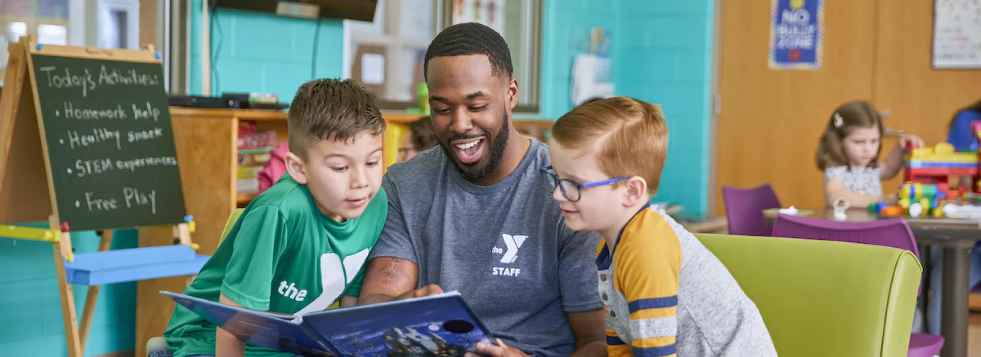 ymca y club staff reading a book to two boys in the ymca y club before and after school program