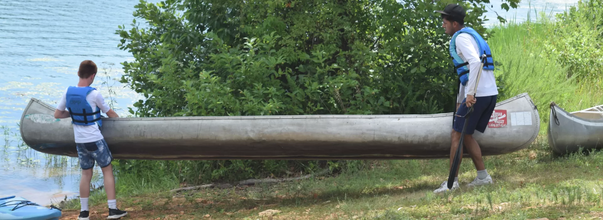 two young men putting a canoe in the lake