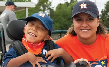 YMCA adaptive sports participant in a wheelchair smiles with his coach buddy